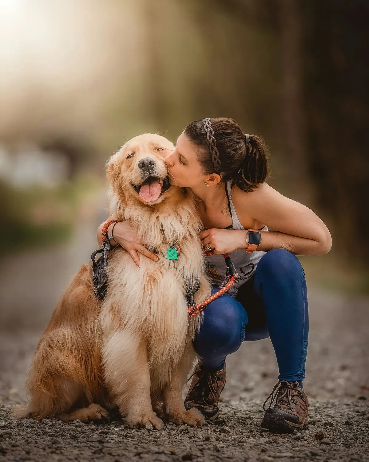 Tutora agachada abraçando e beijando um golden retriever ao ar livre